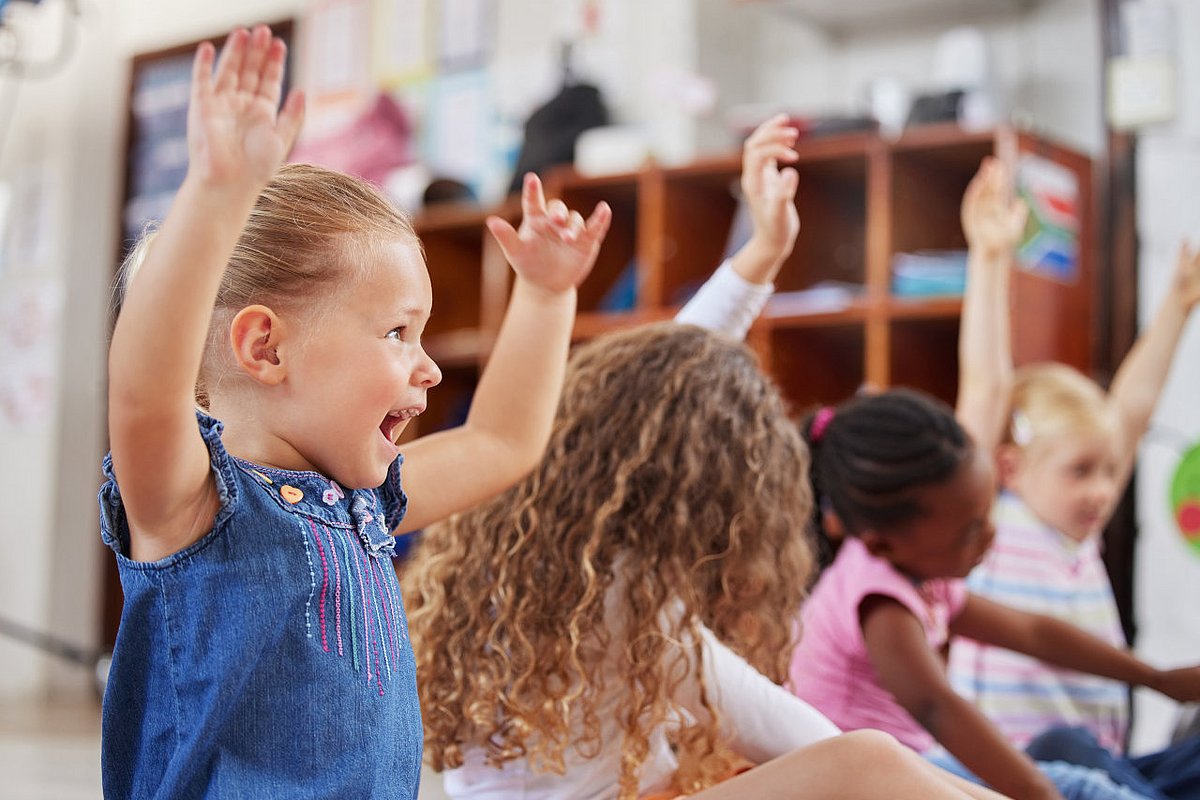 Kita-Kinder sitzen im Kreis und spielen ein Bewegungsspiel. 