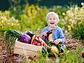 Kita-Kind sitzt im Gemüsegarten und hat einen Korb mit frisch geerntetem Gemüse for sich. 