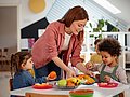 Kita-Kinder essen Obst, eine pädagogische Fachkraft reicht einen Teller an.