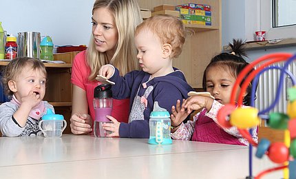 Eine Fachkraft sitzt mit Kita-Kindern am Tisch. 