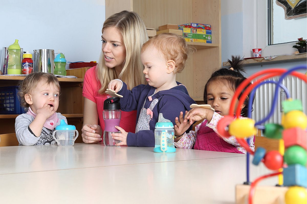 Eine Fachkraft sitzt mit Kita-Kindern am Tisch. 