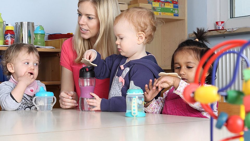 Eine Fachkraft sitzt mit Kita-Kindern am Tisch. 