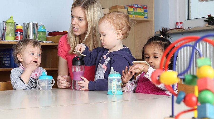 Eine Fachkraft sitzt mit Kita-Kindern am Tisch. 