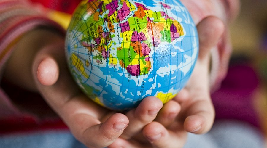 Kleinkinderhände halten einen Spielzeug-Globus.
