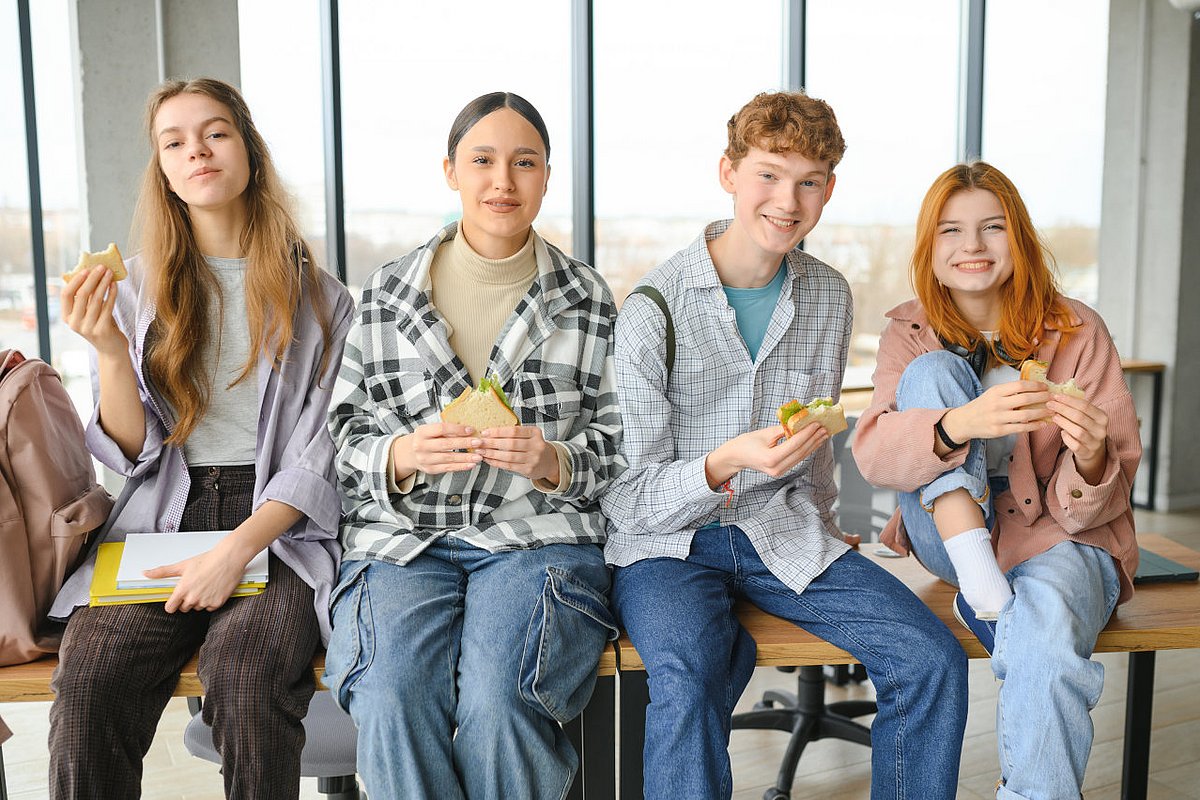 Schüler*innen im Teenageralter sitzen auf einem Tisch und essen Sandwiches.