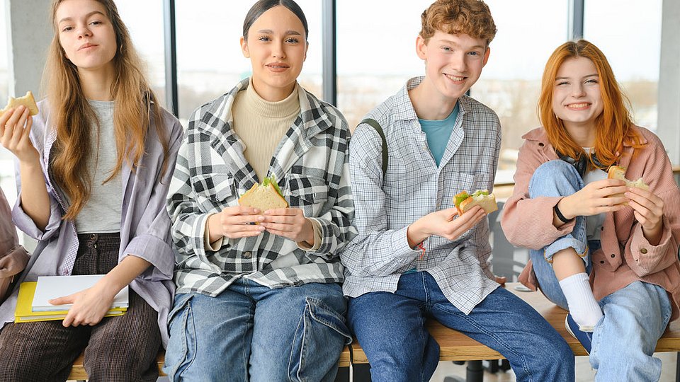 Schüler*innen im Teenageralter sitzen auf einem Tisch und essen Sandwiches.
