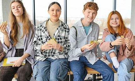 Schüler*innen im Teenageralter sitzen auf einem Tisch und essen Sandwiches.