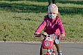 Kleines Mädchen hat pandemiebedingt eine Maske auf und fährt auf ihrem Kinderfahrrad. 