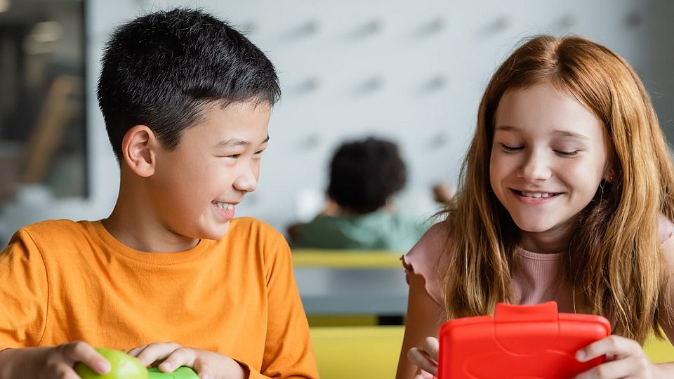 Zwei Schulkinder sitzen in der Schulklasse und essen ihr Frühstück aus der Brotdose. 