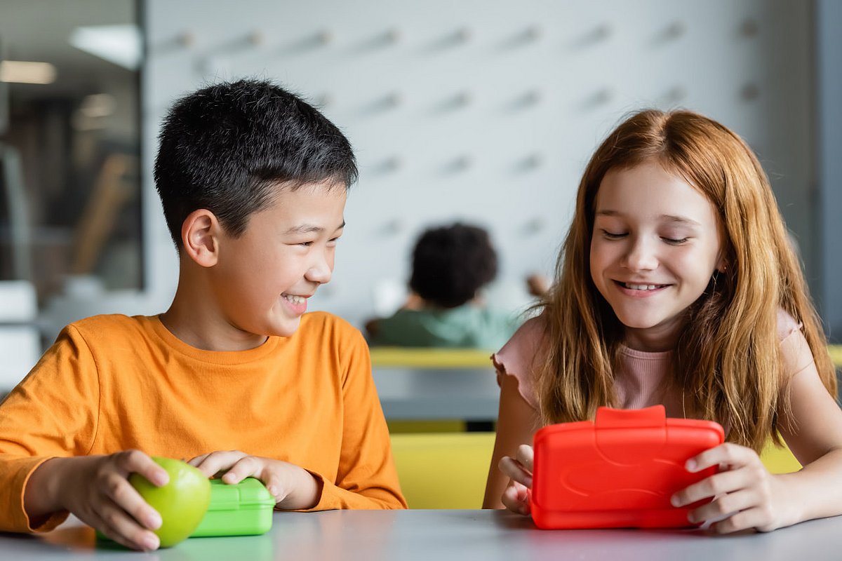 Zwei Schulkinder sitzen in der Schulklasse und essen ihr Frühstück aus der Brotdose. 