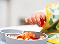 Kleinkind greift mit der Hand Obststückchen aus einer Schale. 