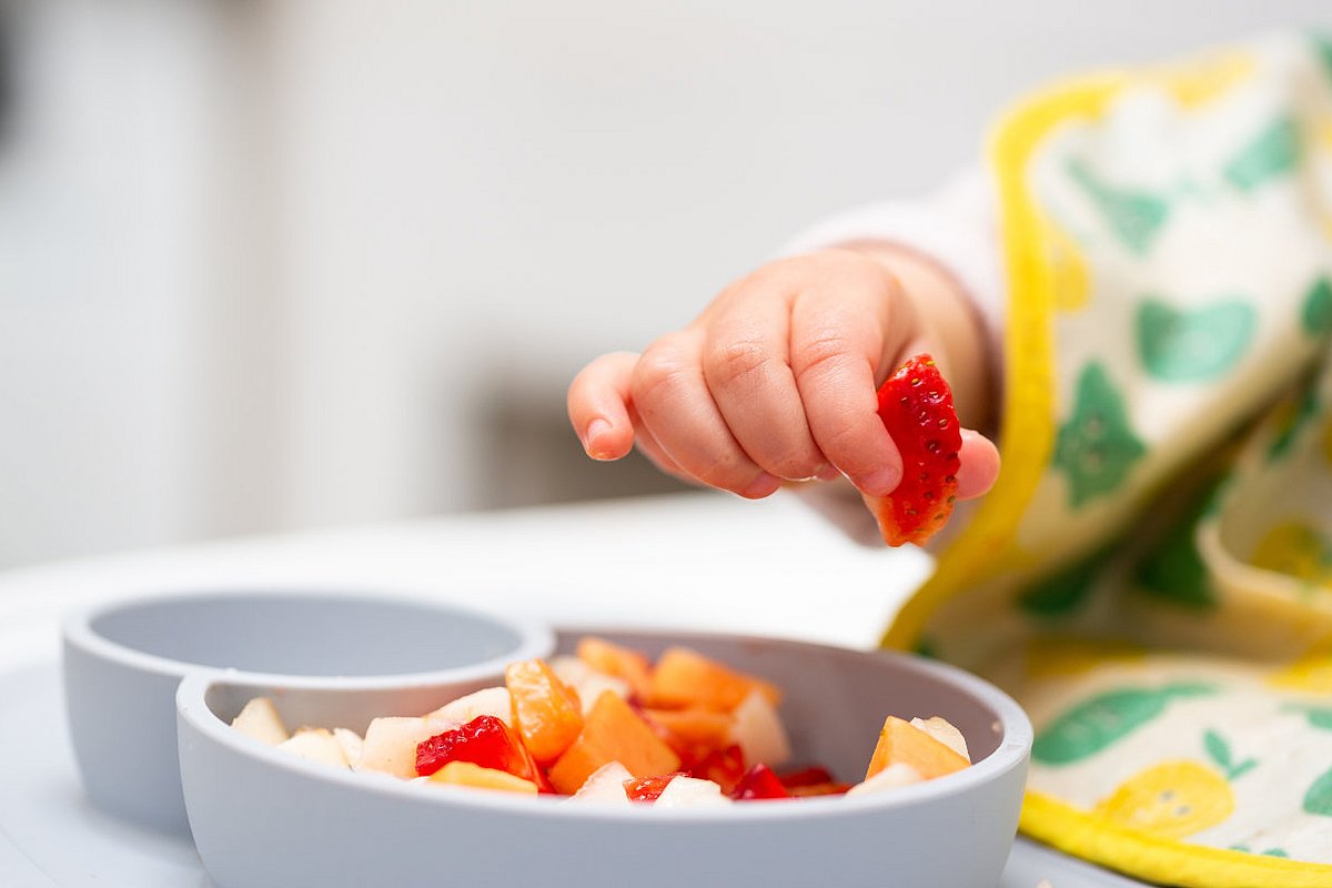 Kleinkind greift mit der Hand Obststückchen aus einer Schale. 