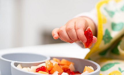 Kleinkind greift mit der Hand Obststückchen aus einer Schale. 