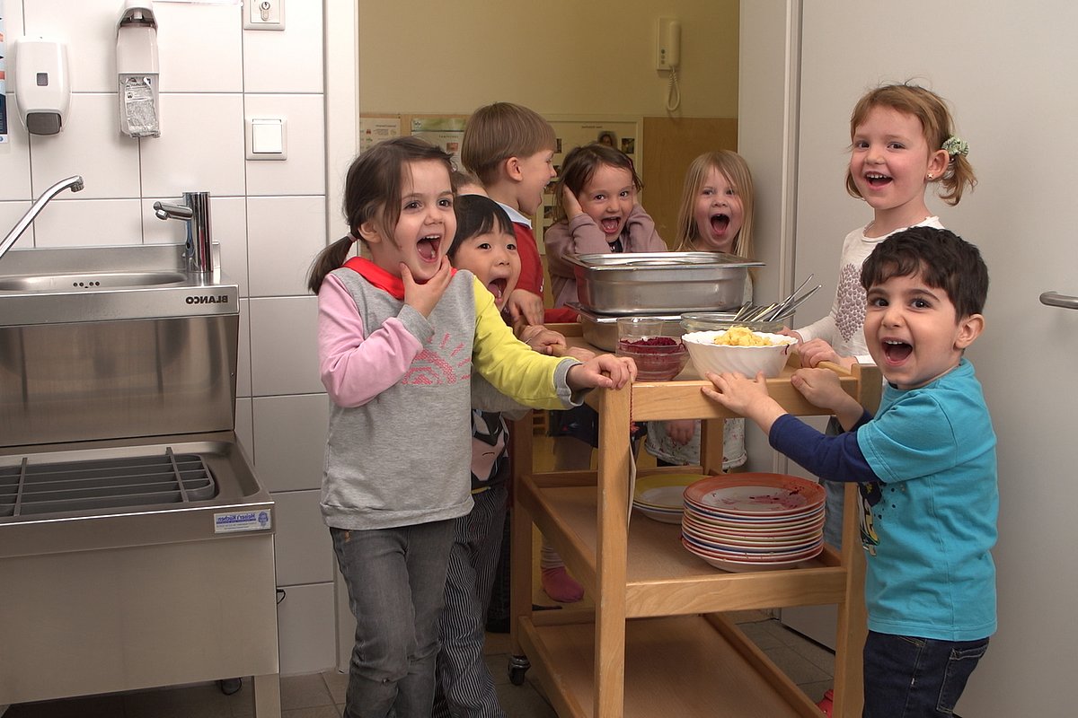 Kita-Kinder bringen schmutziges Geschirr nach dem Essen in die Küche.