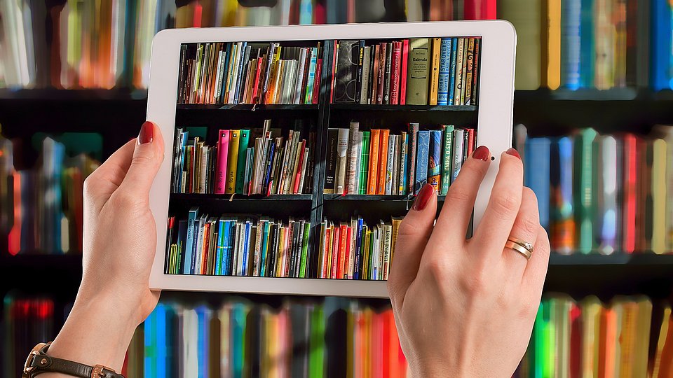 Frauenhände halten vor einem Bücherregal ein Tablet.