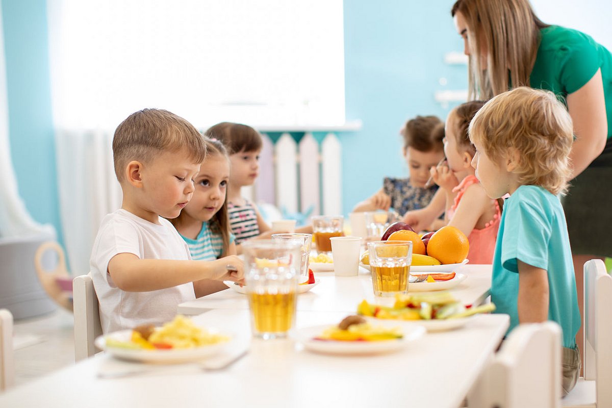 Kita-Fachkraft betreut Kita-Kinder beim Essen.