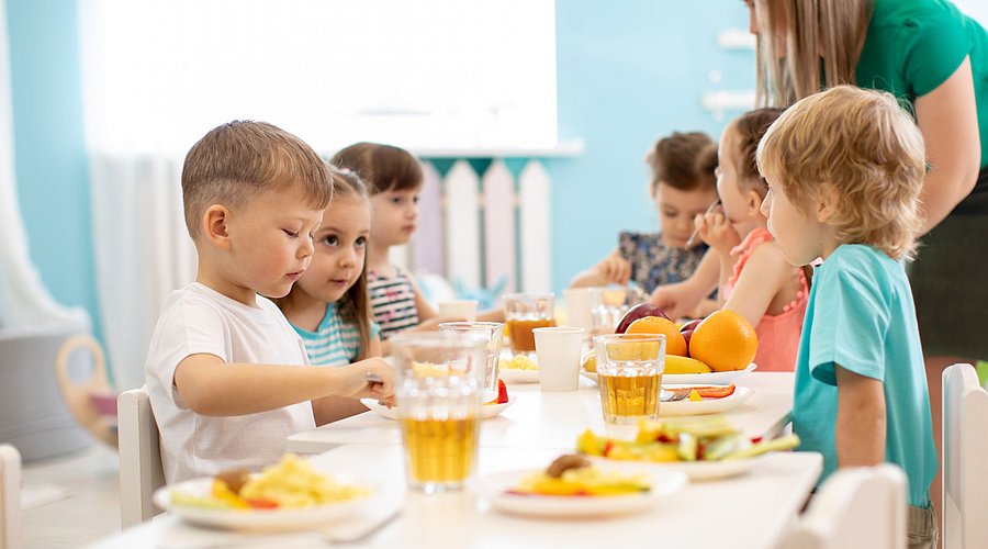 Kita-Fachkraft betreut Kita-Kinder beim Essen.
