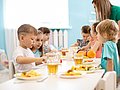 Kita-Fachkraft betreut Kita-Kinder beim Essen.