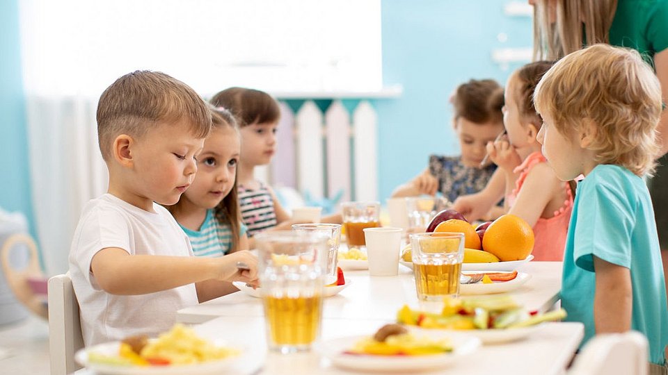 Kita-Fachkraft betreut Kita-Kinder beim Essen.