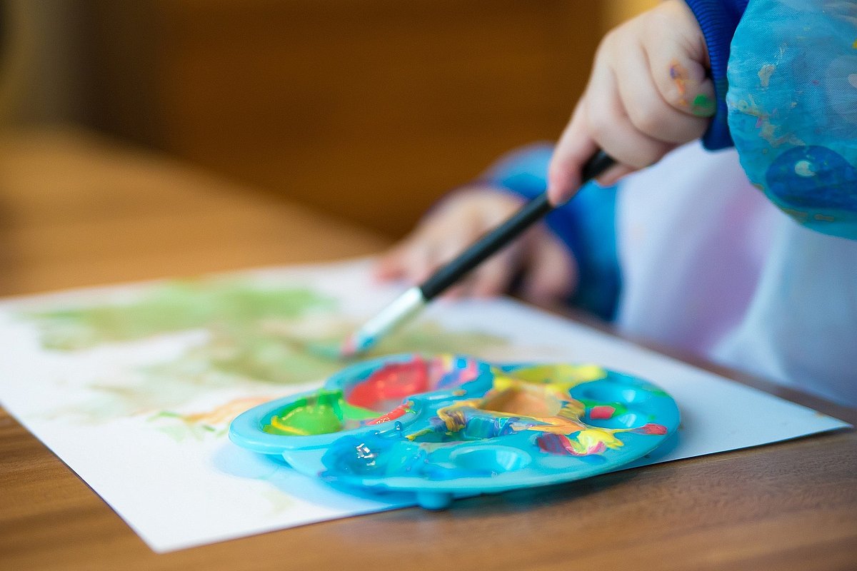 Kind sitzt am Tisch und malt mit Wasserfarben.