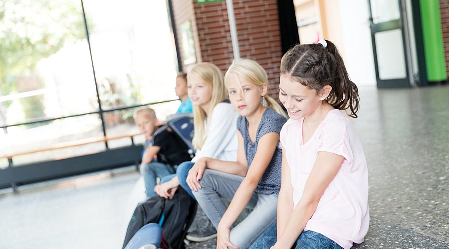 Schulkinder sitzen in einem Schulflur auf der Treppe.