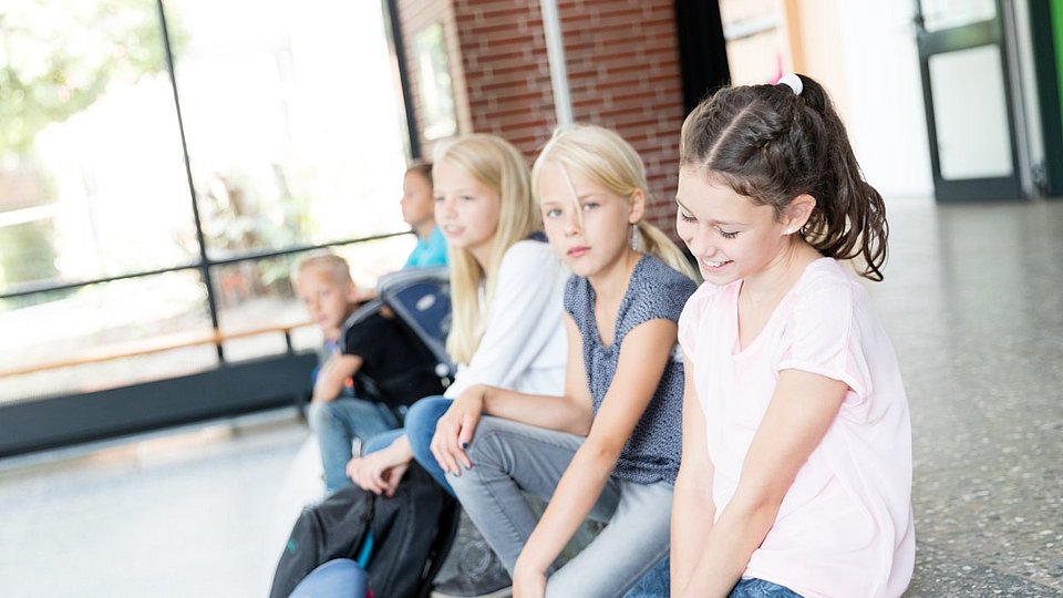 Schulkinder sitzen in einem Schulflur auf der Treppe.