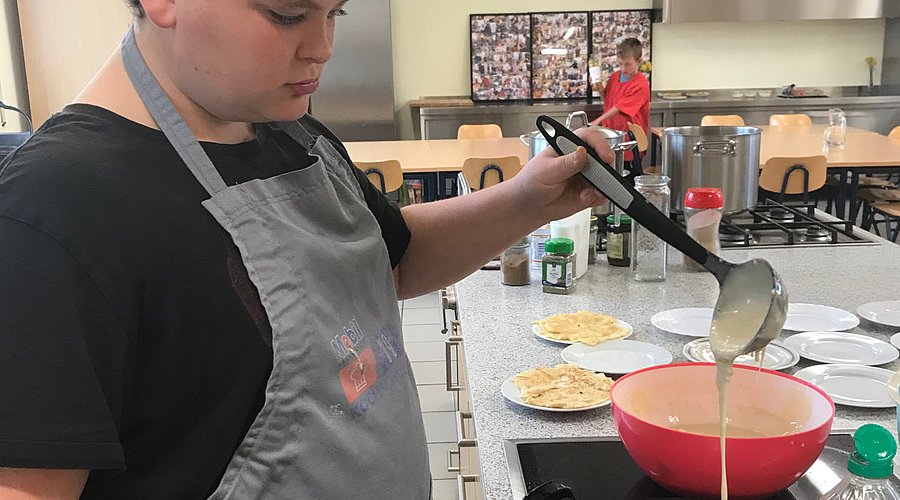 Schüler backt in einer Schulküche Pfannkuchen. 
