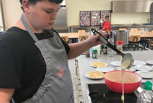 Schüler backt in einer Schulküche Pfannkuchen. 