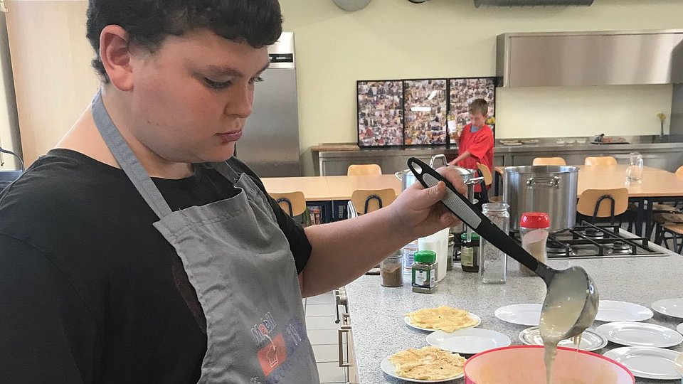 Schüler backt in einer Schulküche Pfannkuchen. 