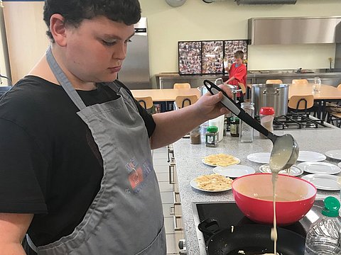 Schüler backt in einer Schulküche Pfannkuchen. 