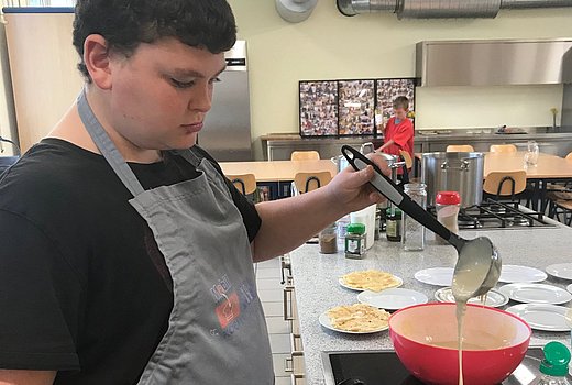 Schüler backt in einer Schulküche Pfannkuchen. 