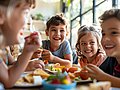 Schulkinder sitzen an einem Tisch in der Mensa und essen. 