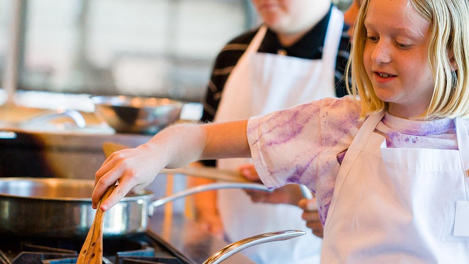 Schulkinder bereiten in einer Lehrküche Essen zu. 