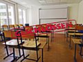 In einem Klassenzimmer sind alle Stühle hochgestellt. Quer über das Bild verläuft ein Banner mit dem Wort "Geschlossen". 