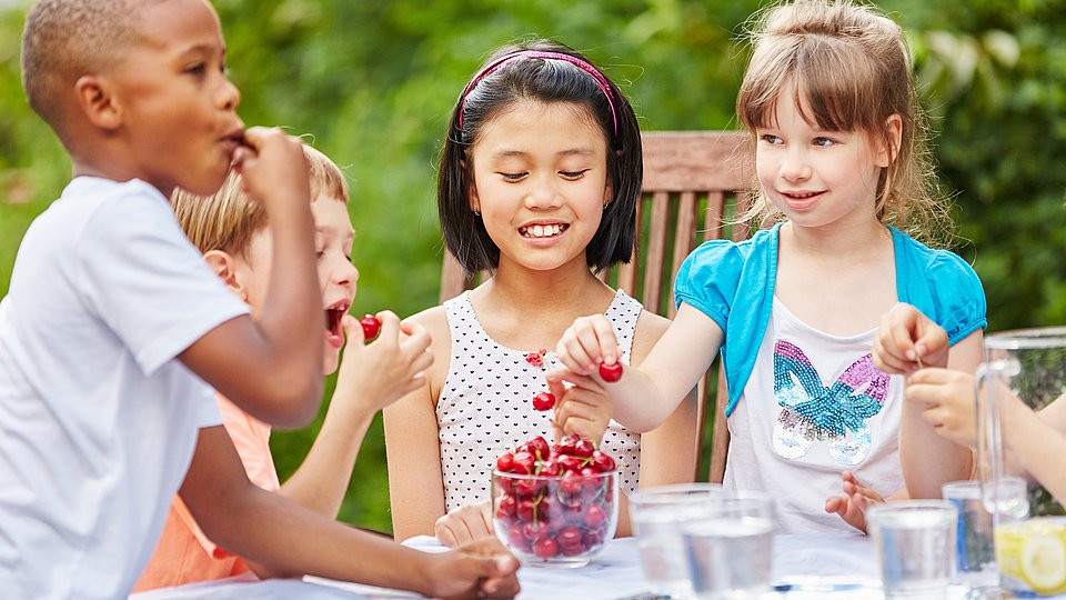 Kinder die zusammen an einem Tisch Kischen essen