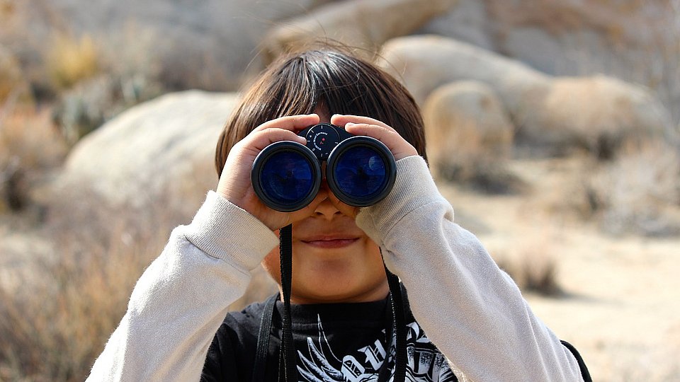 Kind guckt durch ein Fernglas in die Kamera