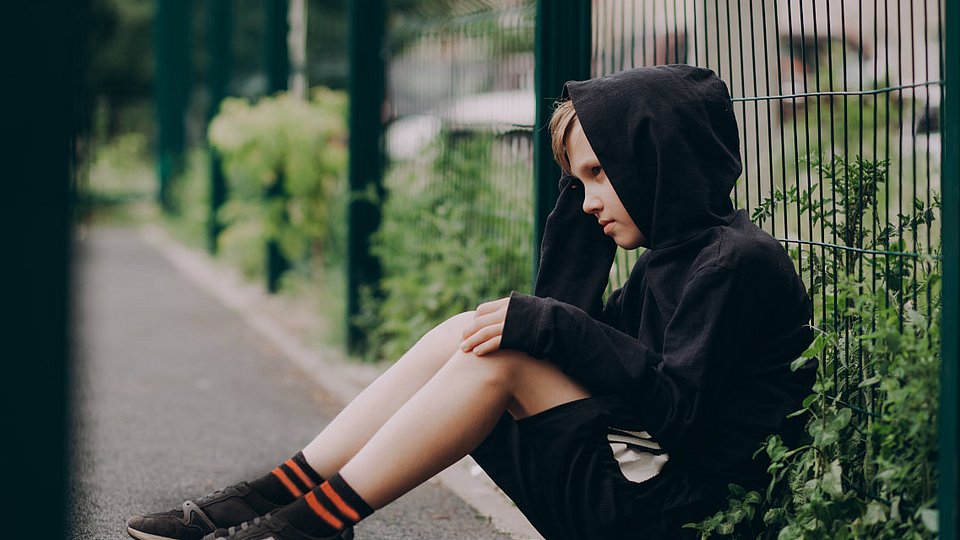 Ein Junge sitzt demotiviert an einen Schulzaun gelehnt.