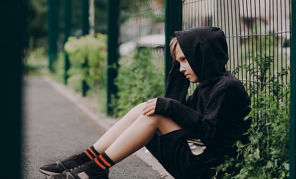 Ein Junge sitzt demotiviert an einen Schulzaun gelehnt.