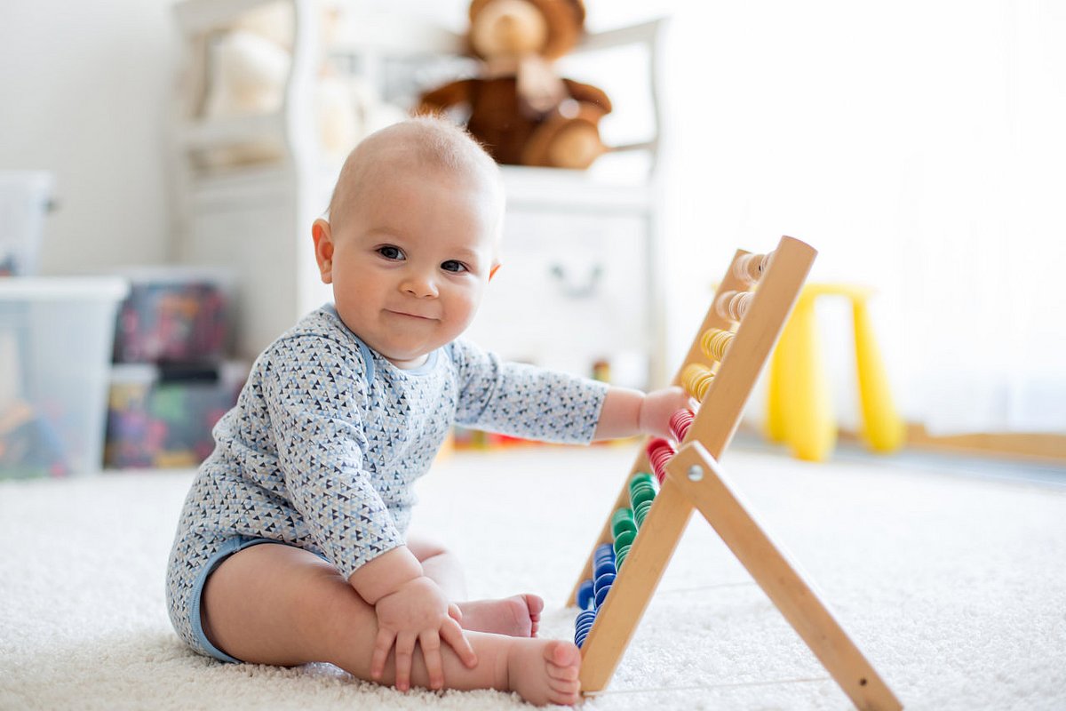 Baby spielt im Sitzen auf einem Teppich mit einem Holzspielzeug. 