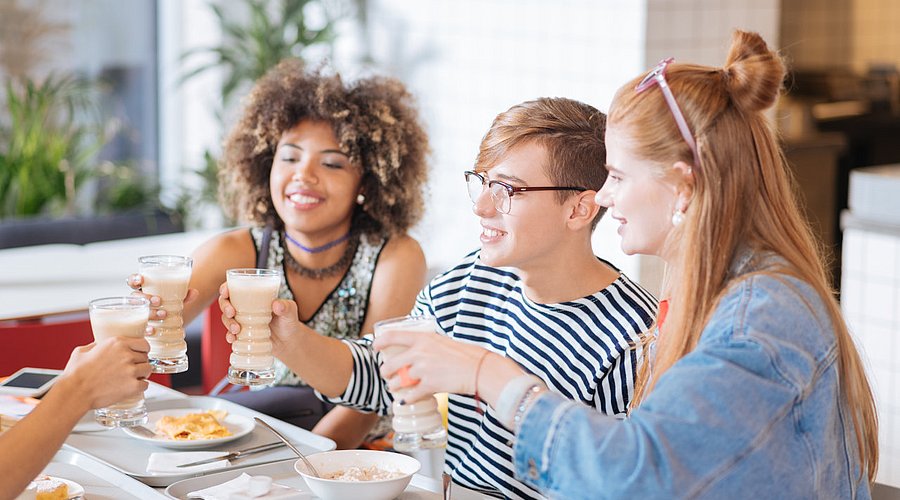 Teenager sitzen in Schulmensa am Tisch und unterhalten sich.