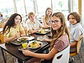 Eine Gruppe jugendlicher Schüler*innen isst gemeinsam in der Mensa. 