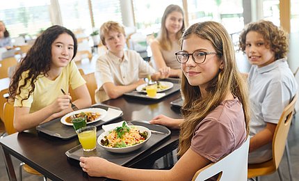 Eine Gruppe jugendlicher Schüler*innen isst gemeinsam in der Mensa. 