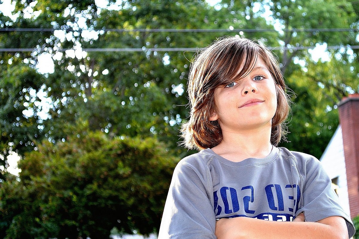 Ein Junge im Teenageralter steht mit verschränkten Armen in einem Garten. 