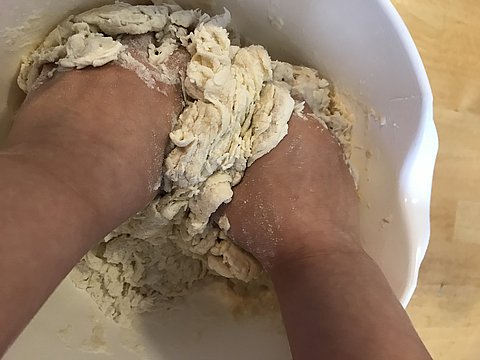 Kind knetet in einer Kita mit beiden Händen Teig in einer Schüssel.