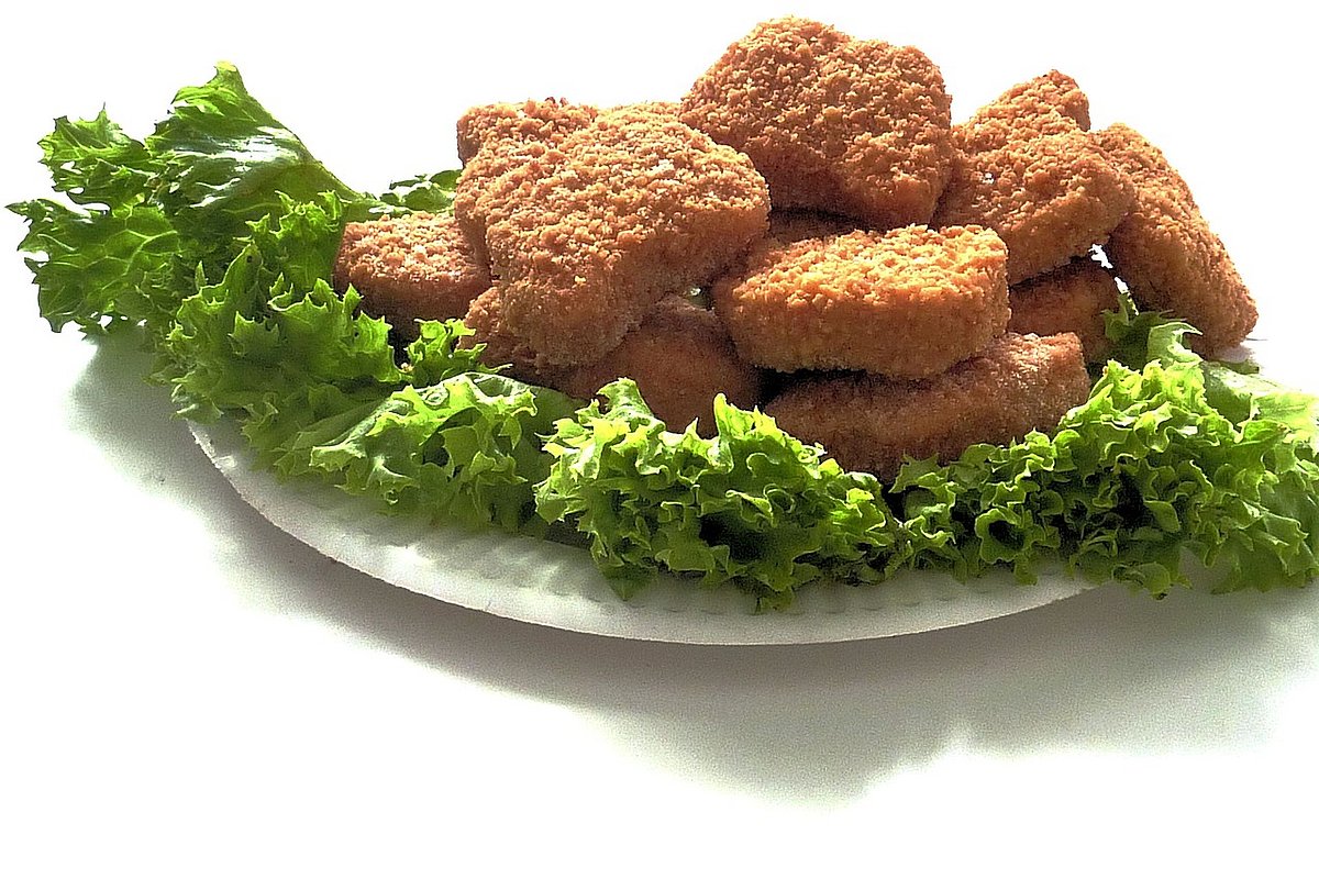 Auf einem weißen Teller liegen Salatblätter und darauf frittierte und panierte Chicken Nuggets.
