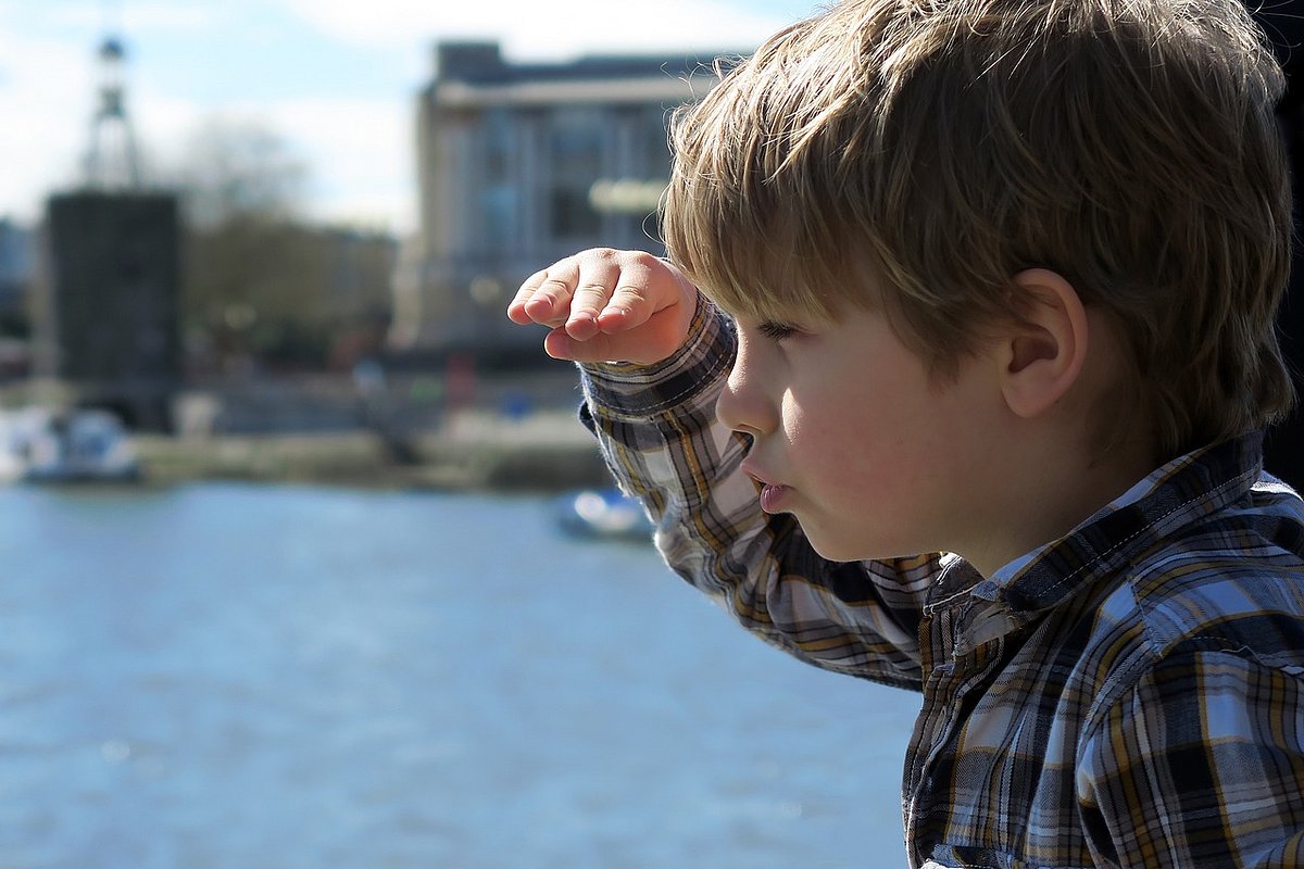 Ein Junge schaut in die Ferne und legt dabei die Hand über die Augen. Im Hintergrund ein See oder das Meer.