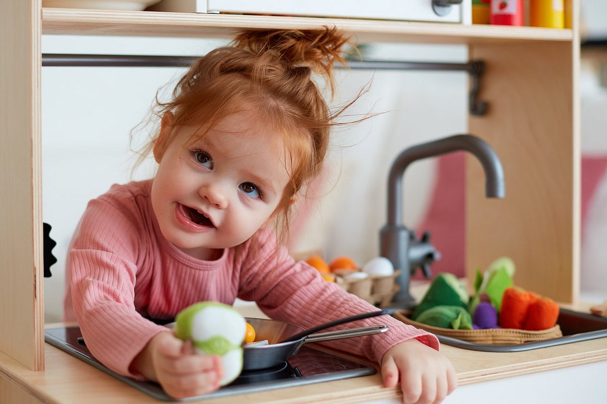 Ein Kleinkind spielt in einer Kinder-K&uuml;che mit Lebensmitteln aus Holz. 