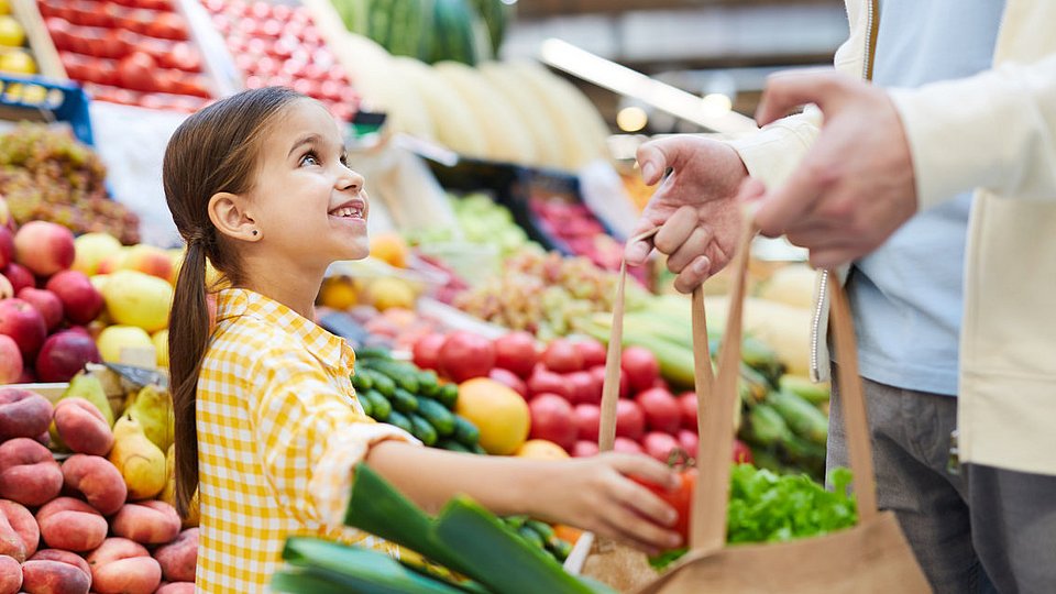Ein Mädchen ist mit ihrem Vater im Supermarkt und wählt Gemüse aus. 