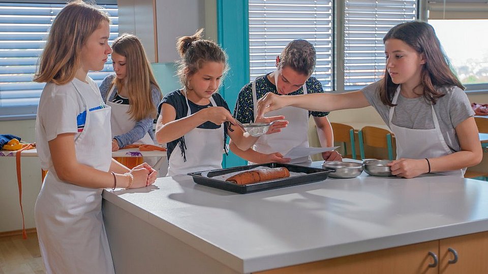 In einer Lehrküche bereiten Schüler*innen einen Kuchen zu. 