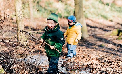 Jungen im Kita-Alter spielen mit Stöcken im Wald. 